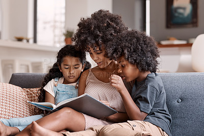 Buy stock photo Shot of a happy young mother reading a book and spending time with her two children at home