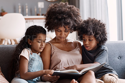 Buy stock photo Shot of a happy young mother reading a book and spending time with her two children at home