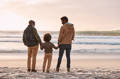 Buy stock photo Rearview shot of an adorable little boy watching the sunset at the beach with his grandfather and father