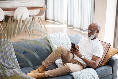 Buy stock photo Shot of a mature man using a cellphone while relaxing on a sofa at home