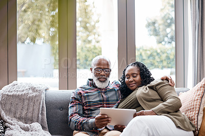 Buy stock photo Shot of a mature couple using a digital tablet while relaxing together on a sofa at home