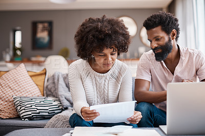 Buy stock photo Shot of a couple looking at paperwork while using a laptop in their living room