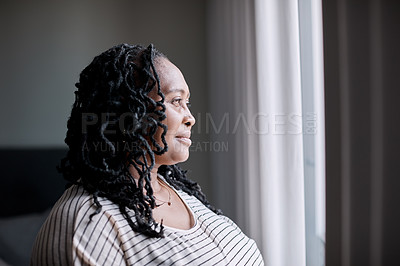 Buy stock photo Shot of a mature woman looking thoughtfully through a window at home