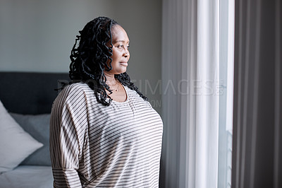 Buy stock photo Shot of a mature woman looking thoughtfully through a window at home