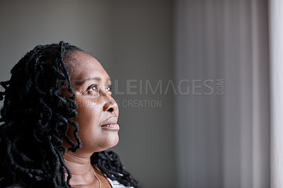Buy stock photo Shot of a mature woman looking thoughtfully through a window at home
