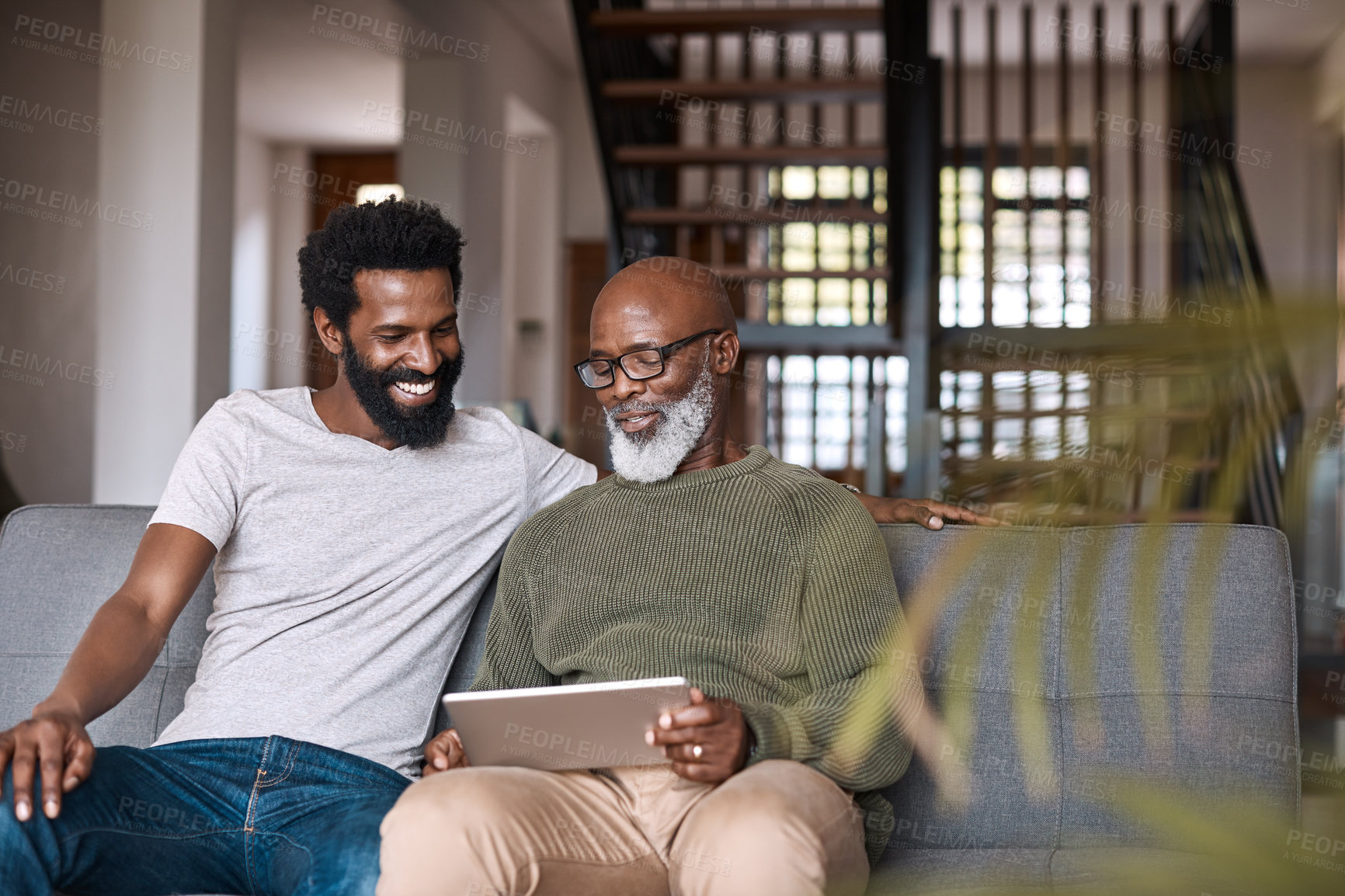 Buy stock photo Shot of a happy senior man using a digital tablet while spending some time with his adult son at home