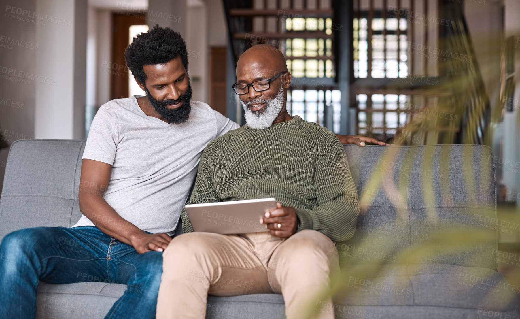 Buy stock photo Shot of a happy senior man using a digital tablet while spending some time with his adult son at home