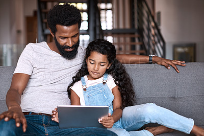 Buy stock photo Shot of an adorable little girl using a digital tablet while bonding and spending time with her father at home