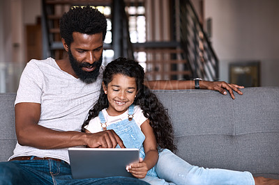 Buy stock photo Shot of an adorable little girl using a digital tablet while bonding and spending time with her father at home