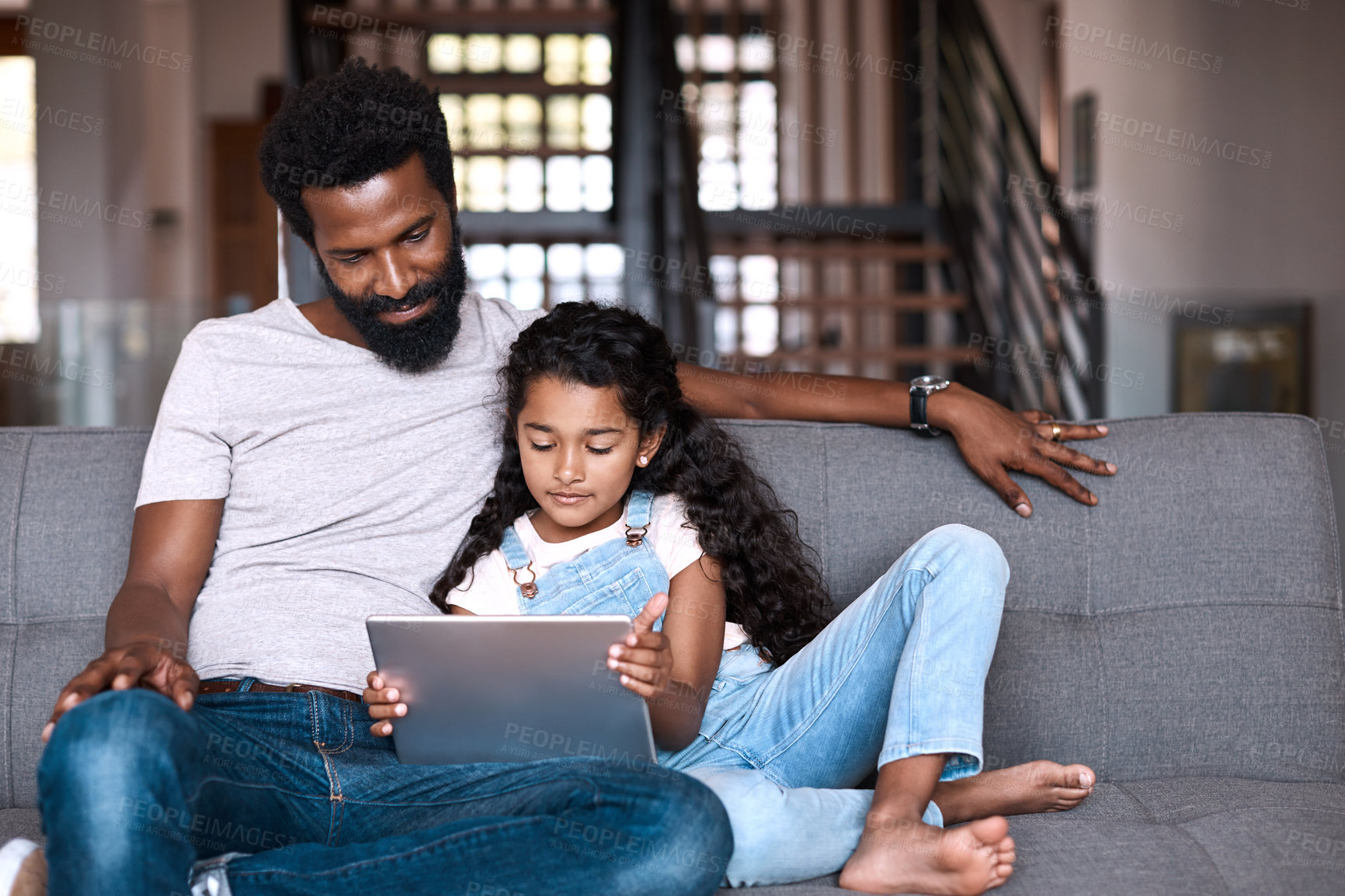 Buy stock photo Shot of an adorable little girl using a digital tablet while bonding and spending time with her father at home