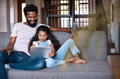Buy stock photo Shot of an adorable little girl using a digital tablet while bonding and spending time with her father at home