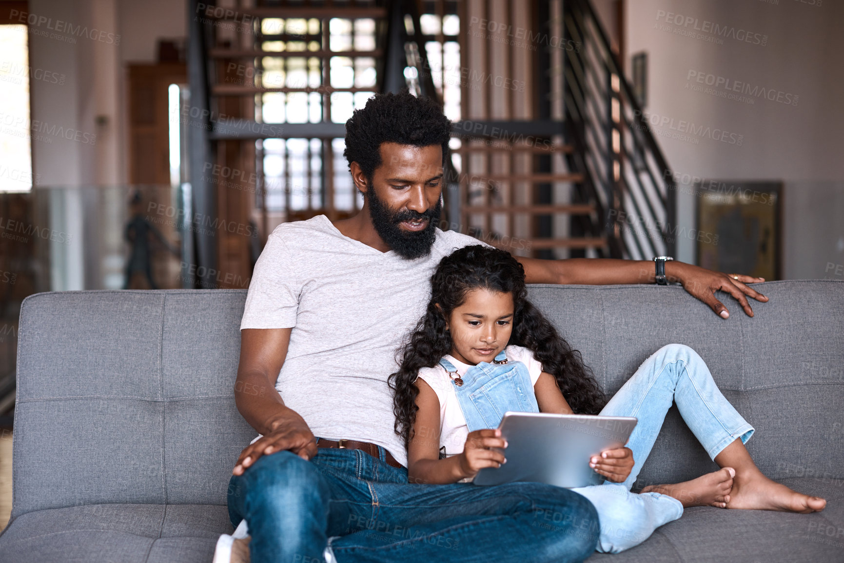 Buy stock photo Shot of an adorable little girl using a digital tablet while bonding and spending time with her father at home