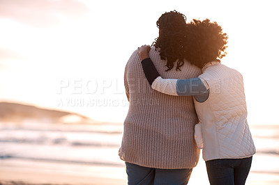 Buy stock photo Rearview shot of a young woman embracing her mother while watching the sunset at the beach