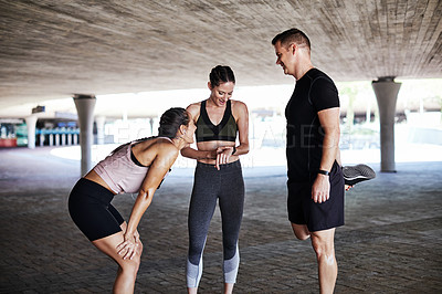 Buy stock photo Cropped shot of three young athletes talking and checking their times while working out in the city
