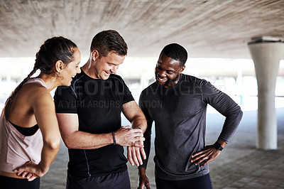 Buy stock photo Cropped shot of three young athletes talking and checking their times while working out in the city