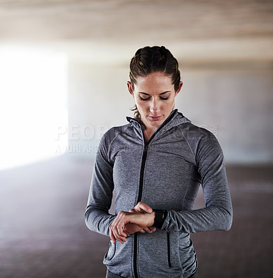 Buy stock photo Cropped shot of an attractive young female athlete checking her watch while working out in the city