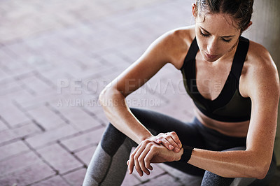 Buy stock photo Cropped shot of an attractive young female athlete checking her watch while working out in the city
