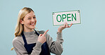 Open, happy and portrait of woman as cafe owner in studio to welcome, announcement or signage. Smile, pointing and advertising for hospitality career, store or waitress with poster on blue background