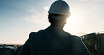 Outdoor, man and back of construction worker on site in city with thinking, ideas or planning renovation. Hardhat, flare and civil engineer with decision on maintenance, building or repairs in town.