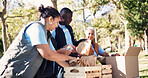 Volunteer, team and packing donation box outdoor with charity manager, outreach and non profit group. People, welfare project and package in park with social responsibility, NGO resources or supplies