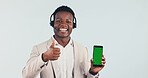 Green screen, call center and black man with thumbs up on phone in studio for crm, contact us or enquiry. Happy, portrait and technical support agent with cellphone and headset on white background.