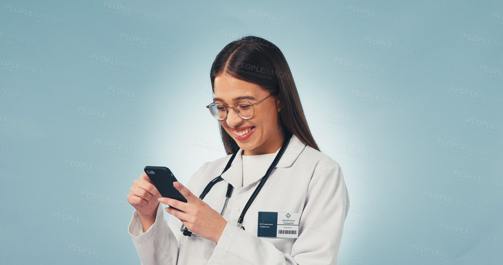 Buy stock photo Happy, woman and doctor with phone in studio with telehealth, consultation or texting on mobile app. Smile, tech and healthcare worker with cellphone for medical research on blue background by space.