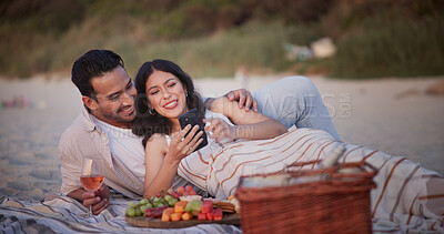 Buy stock photo Couple, picnic and relax on beach with phone, wine and fruit platter with online search for bonding. Happy man, woman and scroll app, internet and charcuterie with drink for break by coast for love