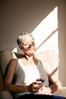 Buy stock photo Shot of a mature woman sitting in her sunny living room drinking a glass of wine