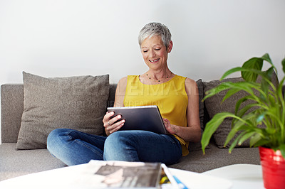 Buy stock photo Shot of a mature woman sitting in her living room using a digital tablet