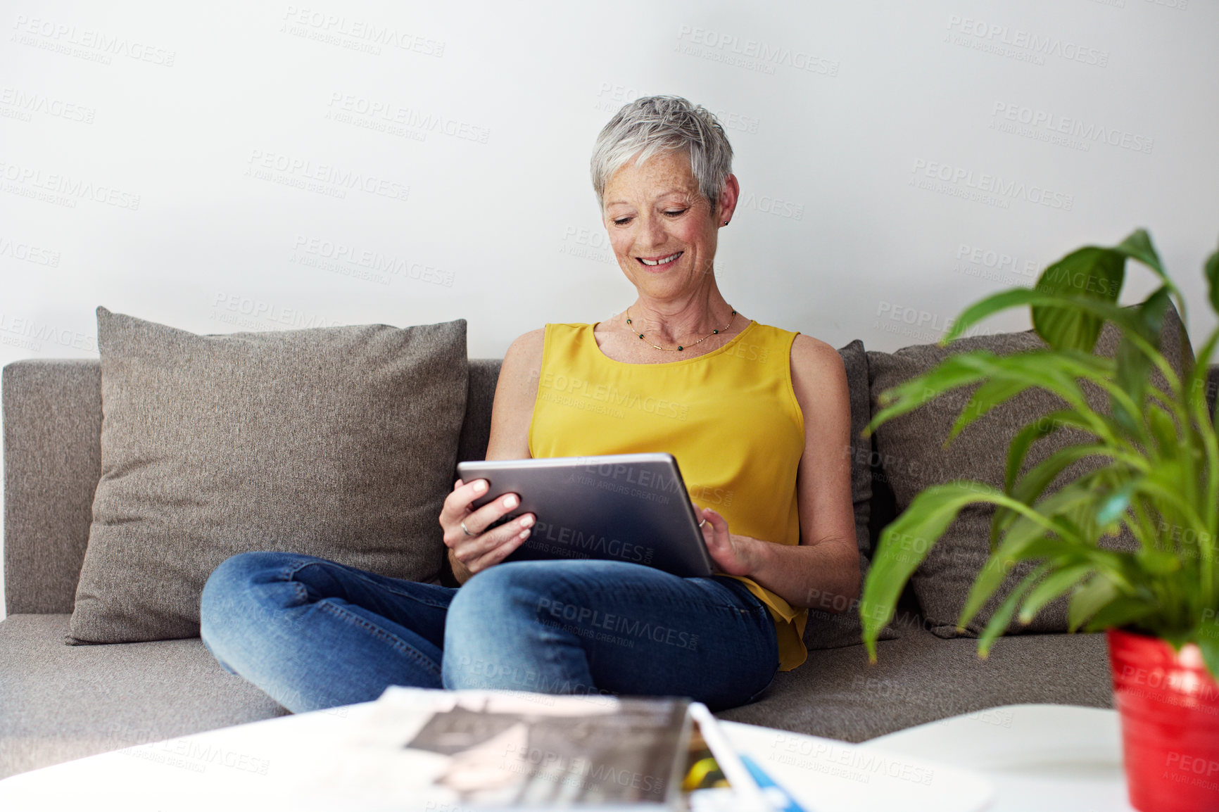 Buy stock photo Shot of a mature woman sitting in her living room using a digital tablet
