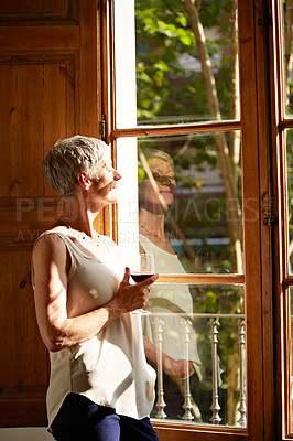 Buy stock photo Shot of a mature woman standing by a window drinking a glass of wine