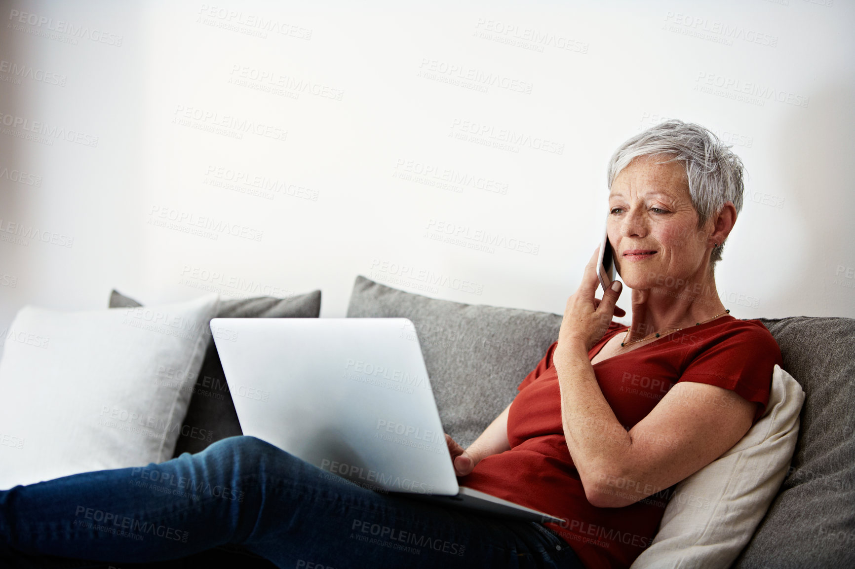 Buy stock photo Shot of a mature woman sitting in her living room using a laptop and talking on the phone