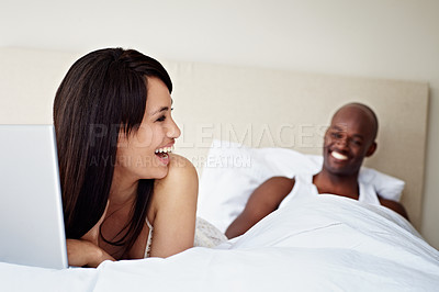 Buy stock photo Shot of a young woman using a laptop while lying in bed with her husband