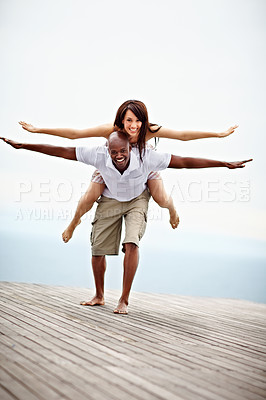Buy stock photo Shot of a man giving his wife a piggyback while walking on a promenade