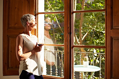 Buy stock photo Shot of a mature woman standing by a window drinking a glass of wine