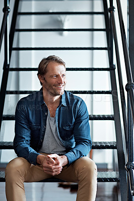 Buy stock photo Shot of a smiling mature man sitting on stairs in his loft apartment