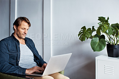 Buy stock photo Shot of a mature man sitting on a chair in his living room using a laptop