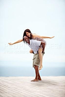 Buy stock photo Shot of a man giving his wife a piggyback while walking on a promenade