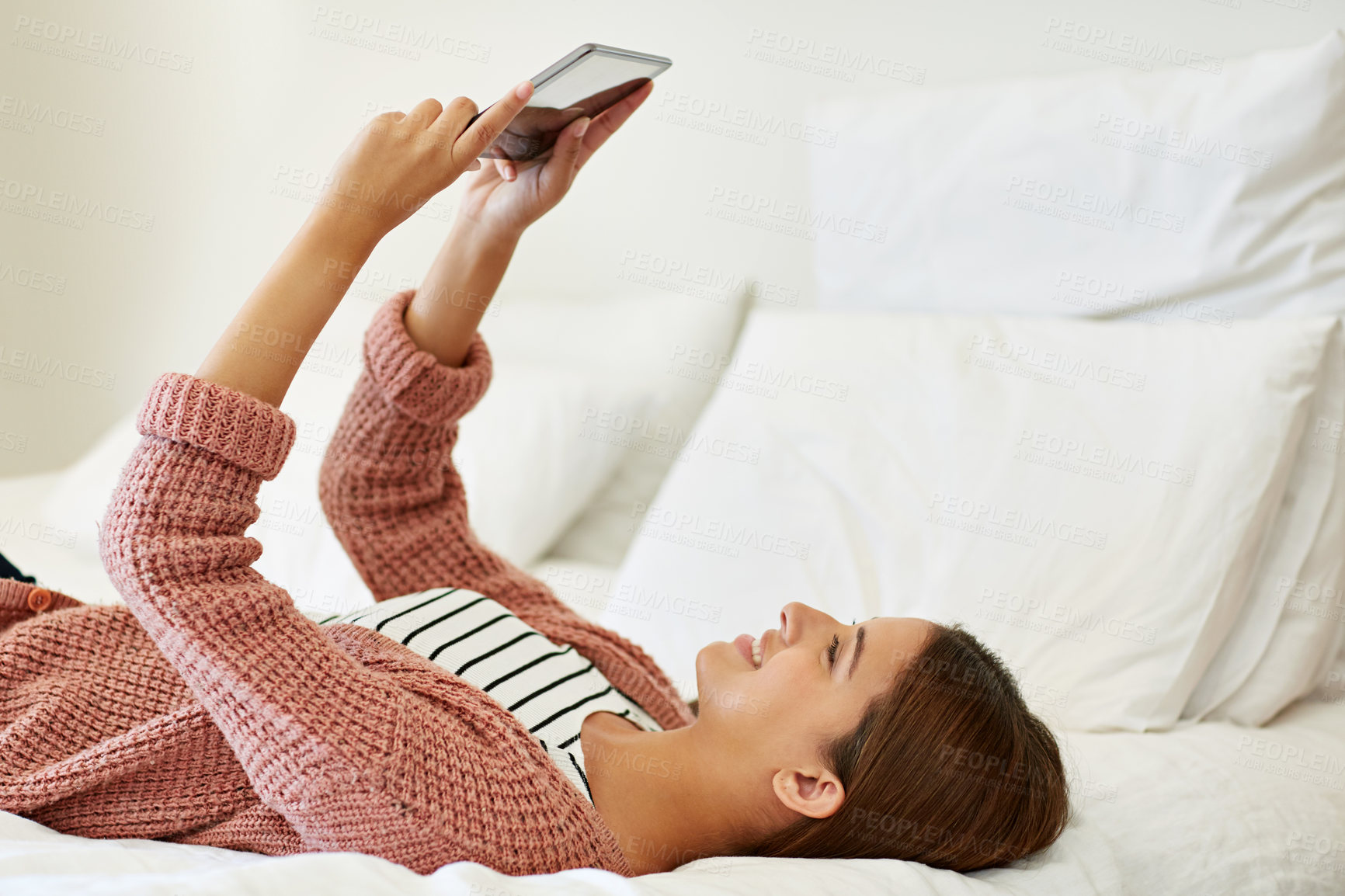 Buy stock photo Shot of a young woman sitting on her bed using a digital tablet