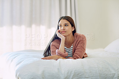 Buy stock photo Shot of a pensive looking young woman lying on her bed