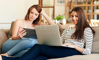 Buy stock photo Shot of two young friends sitting on the sofa using a laptop and digital tablet