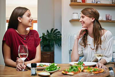 Buy stock photo Shot of two friends sitting at the kitchen table eating pizza and drinking wine