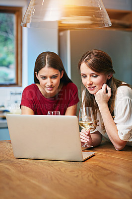 Buy stock photo Shot of two friends sitting at the kitchen table using a laptop and drinking wine