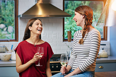 Buy stock photo Shot of two friends laughing together in a kitchen while drinking wine together