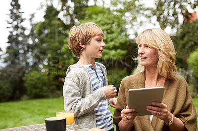Buy stock photo Shot of a grandmother and her grandson sitting at a table in her yard using a digital tablet