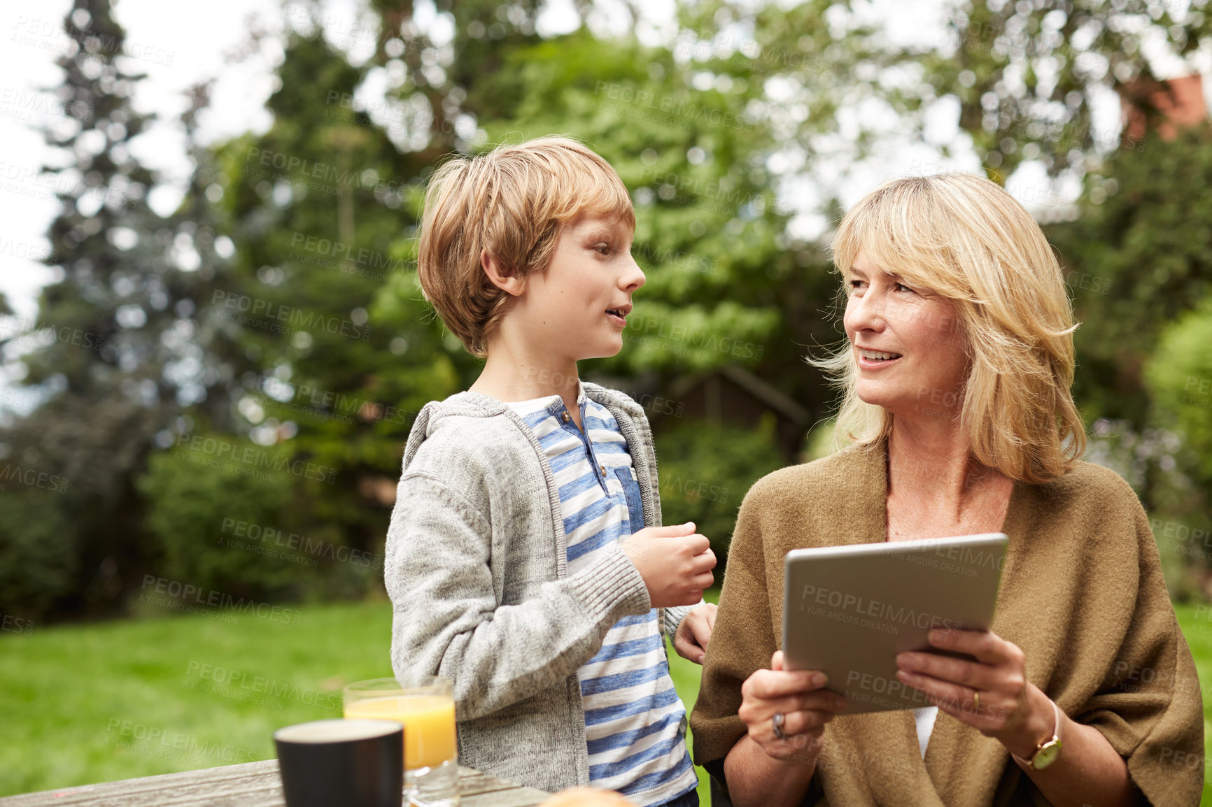 Buy stock photo Shot of a grandmother and her grandson sitting at a table in her yard using a digital tablet