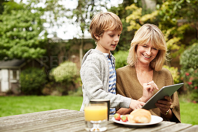Buy stock photo Shot of a grandmother and her grandson sitting at a table in her yard using a digital tablet