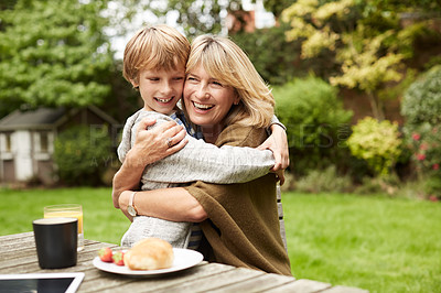 Buy stock photo Portrait of a grandmother and her grandson hugging while sitting at a table in her yard