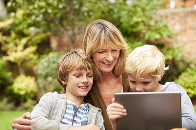 Buy stock photo Shot of a grandmother and her grandsons sitting at a table in her yard using a digital tablet