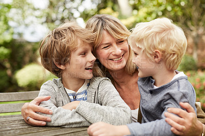 Buy stock photo Shot of a grandmother hugging her grandsons while sitting at a table in her yard